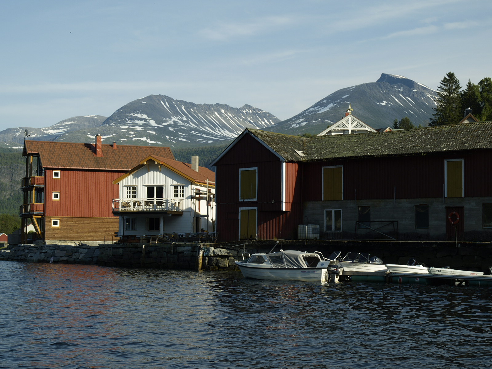 Pakkhuset og nabobygningene ved sjøen på Todalsøra, med båter ved kaia og fjell bak